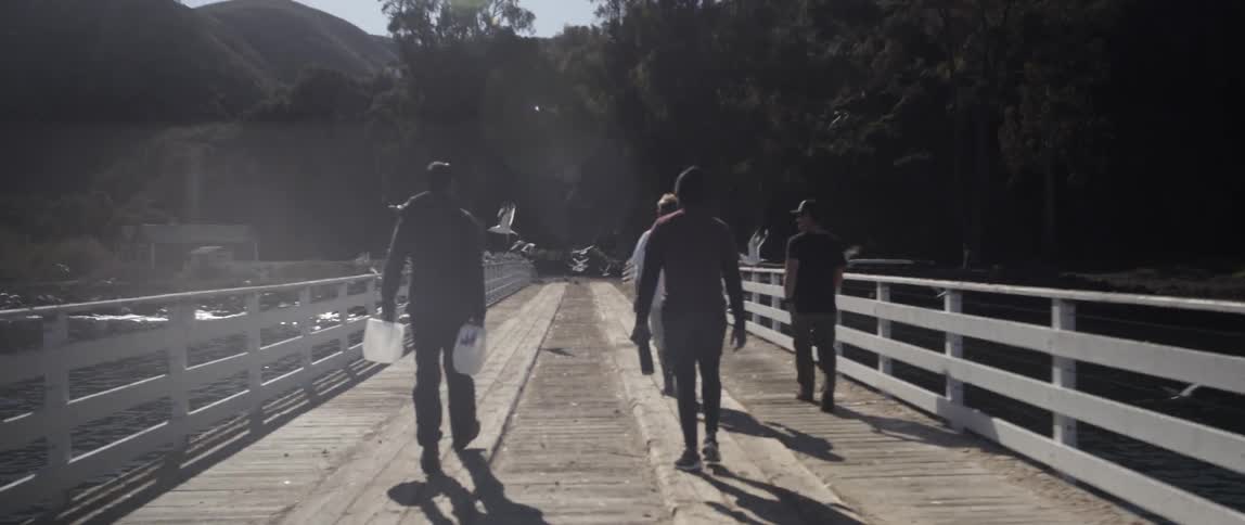 Men walk across a bridge with seagulls flying around