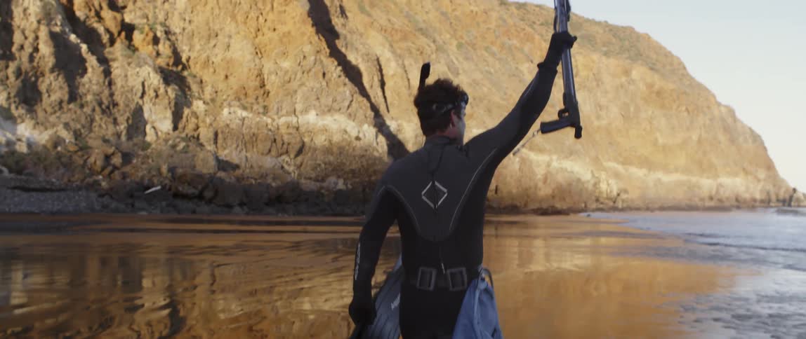 A man in scuba gear walks towards the water