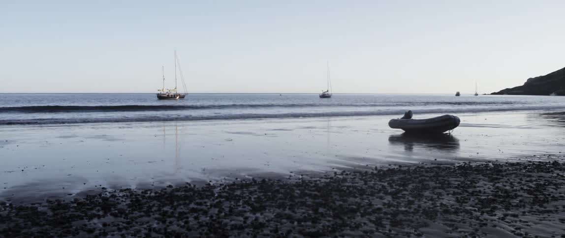 A raft is on the sand of a beach as boats are in the water