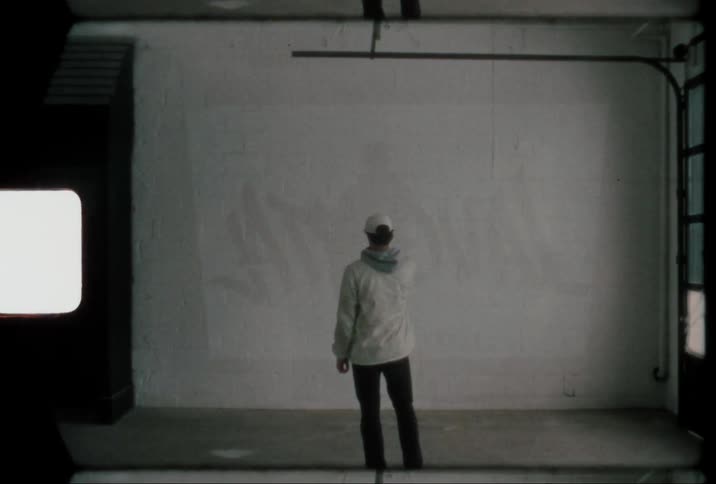 Man with his back facing the camera wearing a cap looking at a blank wall