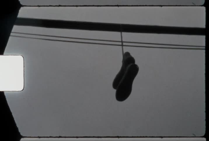 A pair of sneakers are tied together by the shoelaces and hang from a power line