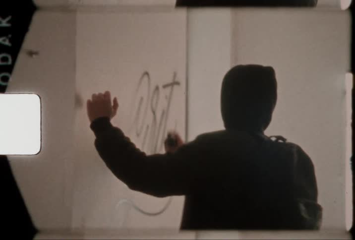 Man in a hoodie with a backpack on his back creating art with black spray paint on a white wall