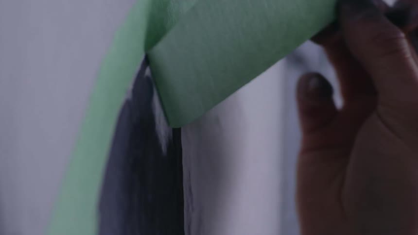 A human hand with a pen between its fingers is pulling a ribbon off the wall