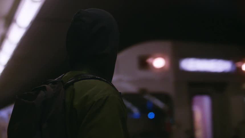 Man with his back facing the camera and carrying a backpack inside a train station where a train is passing by