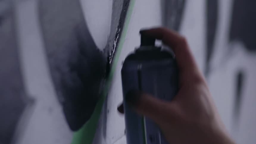 Close up of a person using a spray paint can to paint a white brick wall with black paint