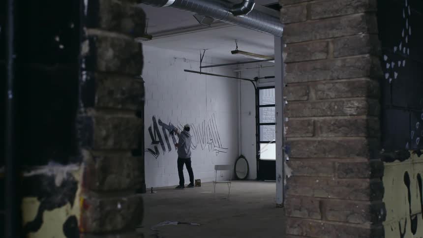 A man in a cap painting letters on a white wall