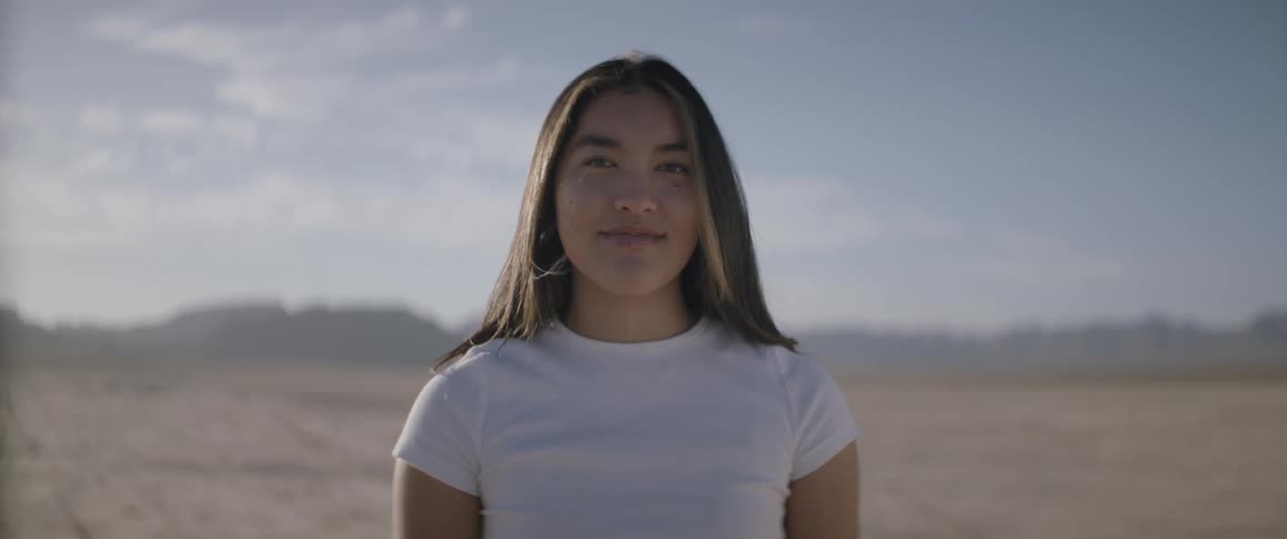 Young woman stands smiling on arid plain with mountains on the horizon