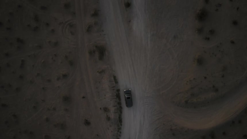 Car drives along dirt road through arid scrubland passing several intersections