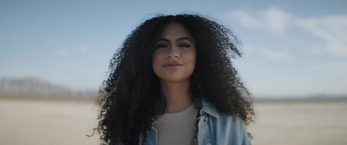 Woman with dark curly hair models and smiles standing outdoors