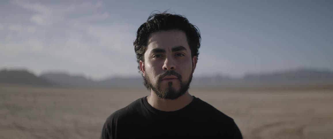 Man stands outdoors on windy plain with mountains in the distance