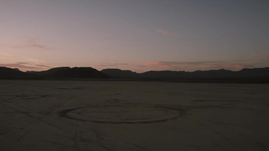 A desert region with mountains in the background and in the sky the sun is rising