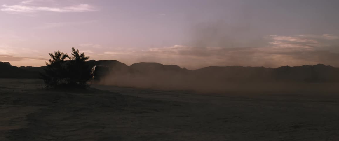 An all terrain vehicle drives across a desert road at dusk