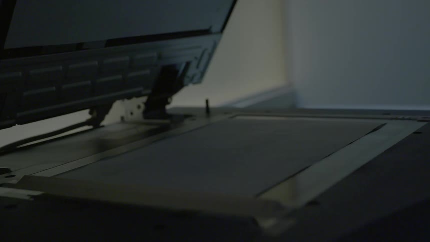 A person presses with his finger a button of a scanner that makes a beam of light on top of a flha of paper