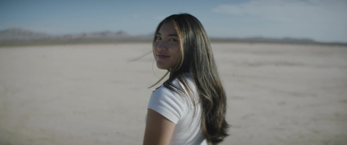 Woman with long dark hair turns away from the horizon to look back