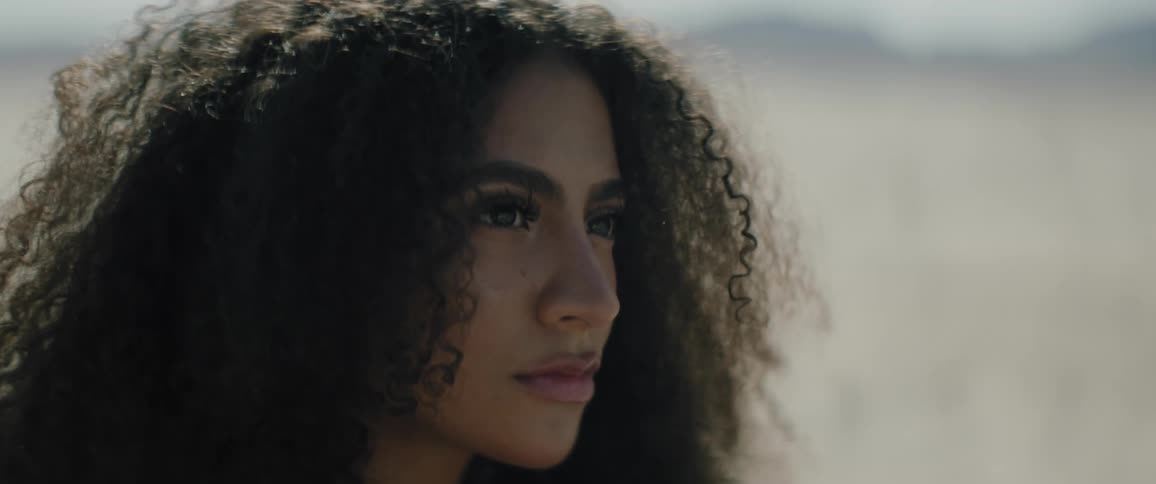 A black woman is looking forward with determined gaze as her hair stirs in the wind