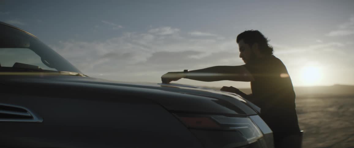 A man walking around the front of his car looking at a map as the sun sets on the horizon