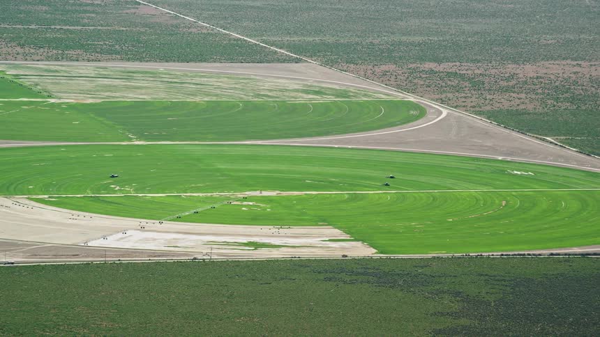 Aerial footage of circular crop fields tractors and Cedar Fort Utah captured during a sunny day in the Southwest United States