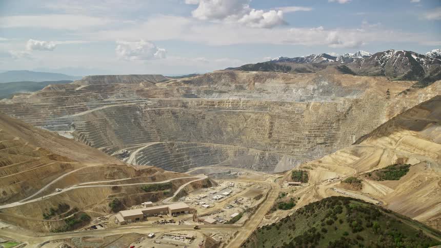 Aerial footage of Bingham Canyon Mine (Kennecott Copper Mine) Utah showcasing the terraced rock bed with buildings on the top plateau during the day