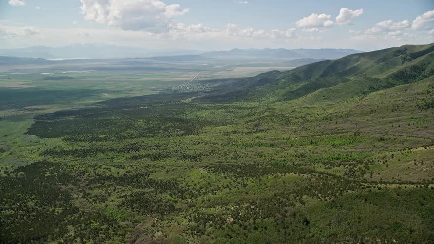  aerial footage captures the breathtaking view of green hills and the Oquirrh Mountains in Utah on a partly cloudy day during summer