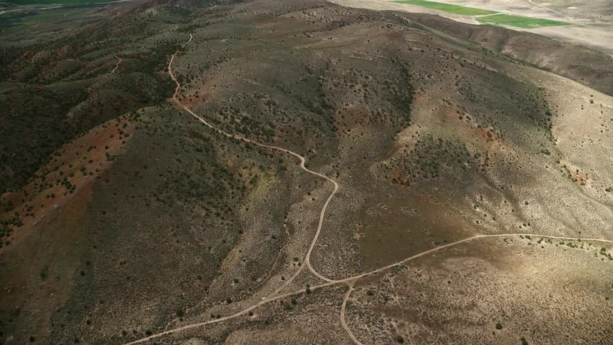 Aerial footage of flying over dirt roads in dry hills in Sterling Utah during a partly cloudy day