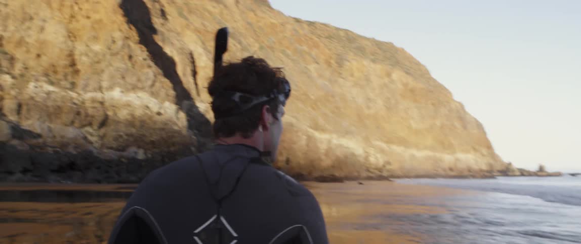 A man in a wet suit is walking on the beach