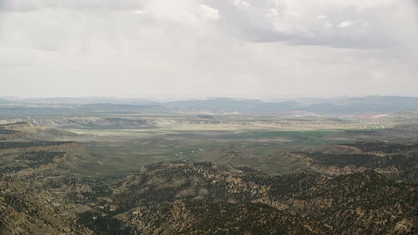 A stunningaerial footage of flying over a green valley with mountain ridges in Grand Staircase-Escalante National Monument Utah on a partly cloudy day in summer showcasing the extensive vegetation and beauty of the Southwest United States