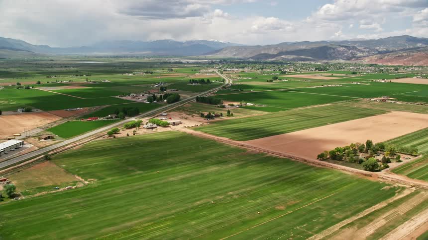 Aerial footage of a vast rural area with mountains on the horizon flying over farmland near Route 118 and approaching the rural town of Richfield Utah during summer