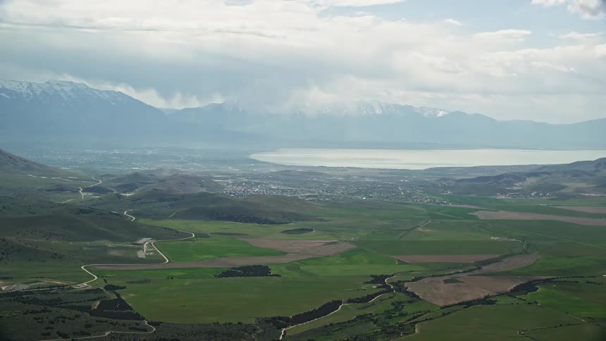Aerial footage of green farmland and Utah Lake in Utah showing rustic agricultural fields and a water body in the southwest landscape during the daytime