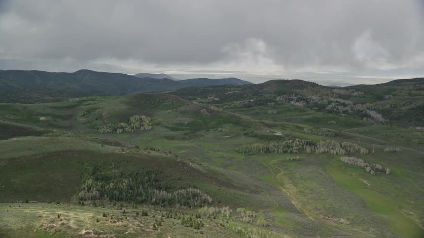 Aerial footage of green hills trees and heavy clouds above the Wasatch Range in Utah during a cloudy summer day