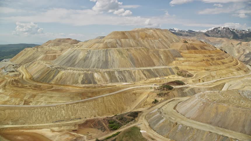 Aerial footage of Bingham Canyon Mine (Kennecott Copper Mine) Utah showcasing its open pit mining operations and terraced mountain with roadways on a bright sunny day