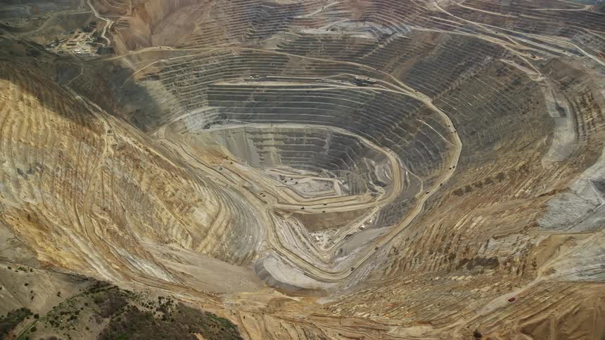  aerial footage orbiting gravel haulers at the Kennecott Copper Mine aka Bingham Canyon Mine in Utah showcasing the immense scale of the open-pit mine during a partly cloudy day