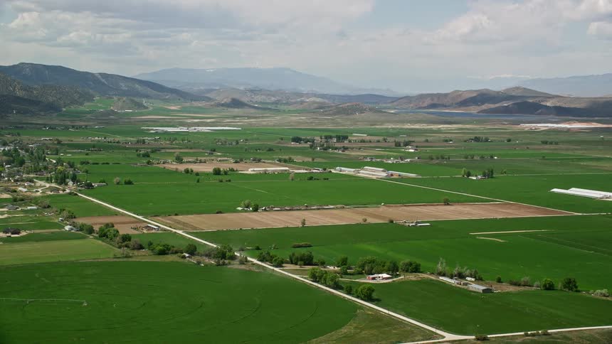 aerial footage of picturesque farmland and majestic mountain ranges as the viewer approaches Manti Utah showcasing the beauty of rural landscape and agriculture in Utah's southwest region during sunny summer days