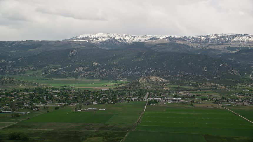 Aerial footage captures a small rural town with the snow-capped peaks of the Wasatch Range in the background in Ephraim Utah during the summer