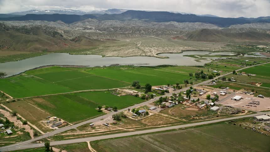 Aerial footage showcasing a rural town with farmland Rocky Ford Reservoir and scenic views of mountains in Sigurd Utah on a partly cloudy day during summer