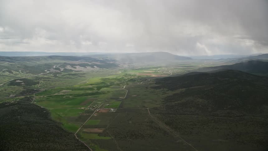 Aerial footage of a lush green farming town nestled in a valley surrounded by mountains in Burrville Utah capturing the beauty of rural life in the Southwest during summer