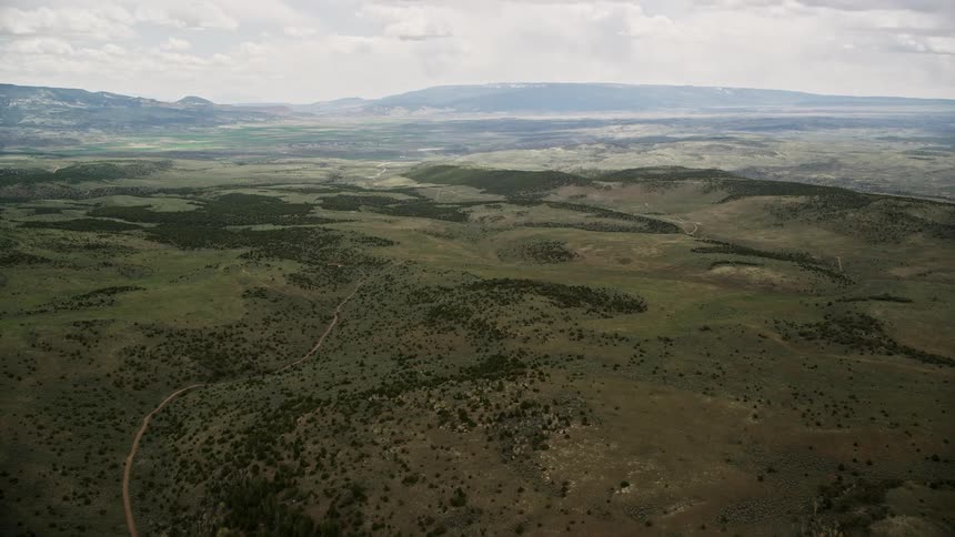 Aerial footage of lush green hills trees and a country road in Fishlake National Forest Utah with cloudy skies and a southwest perspective