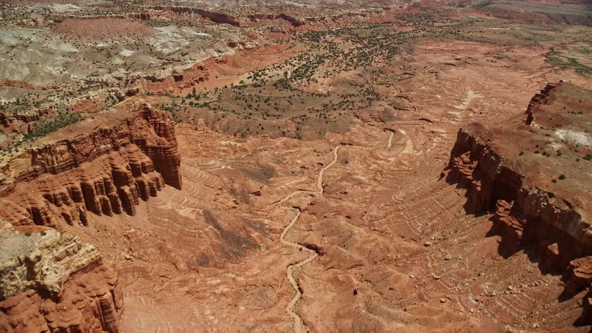 Aerial footage of flying over a dry riverbed through a canyon between mesas showcasing the stunning landscapes of Capitol Reef National Park in Utah during summer