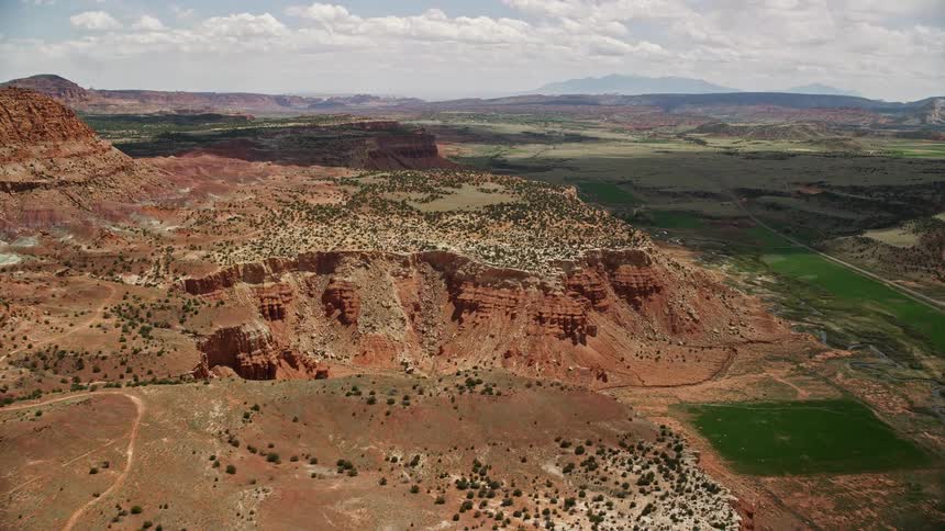 Approaching a famous mesa surrounded by farmland in Capitol Reef National Park Utah in stunningaerial footage