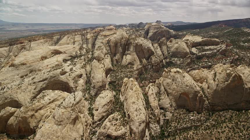 Aerial footage flying towards rock formations of Waterpocket Fold in Capitol Reef National Park Utah on a partly cloudy day showcasing the famous desert landscape of the Southwest United States during summer