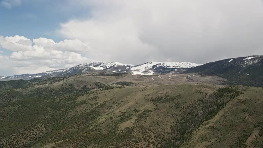 Aerial footage of snow-capped green mountains in Fishlake National Forest Utah with partly cloudy skies