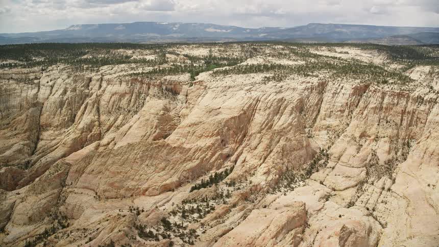  aerial footage flying over a canyon in Grand Staircase-Escalante National Monument Utah showcasing narrow rock formations pine forests and partly cloudy skies in the background