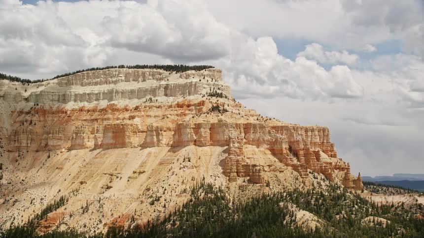 Aerial footage of Barney Top Mesa in Utah showcasing a mesa with desert vegetation and trees set against a backdrop of mountains and partly cloudy skies