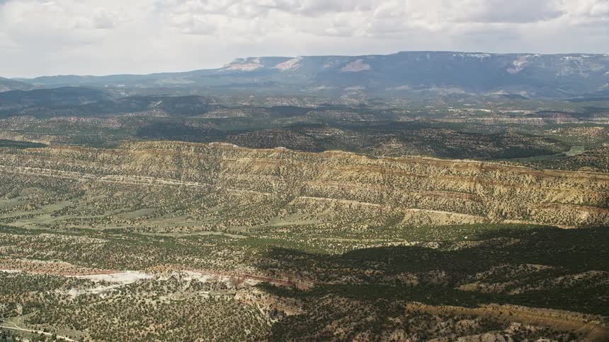 an aerial view of mountain valleys with lush trees lining the plateau and majestic ridges defining the landscape as seen while flying over Grand Staircase-Escalante National Monument in Utah during a partly cloudy day in summer