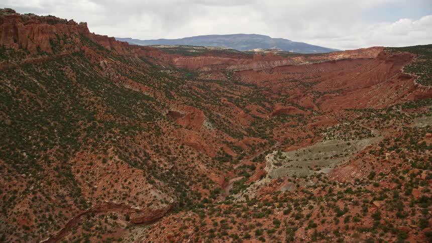 Aerial footage of a deep canyon in Capitol Reef National Park Utah including the approach and fly down showcasing the arid and famous landscape with striations and vegetation along the valley under partly cloudy skies