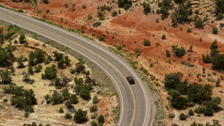 Aerial view of a black SUV driving on Route 12 in Boulder Utah during a partly cloudy day in the Southwest United States