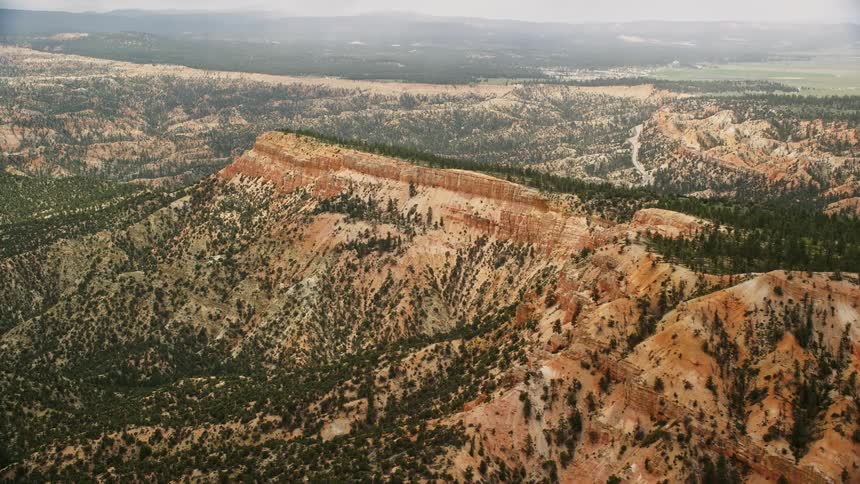 Aerial footage of flying over a long mesa with trees and desert vegetation in Bryce Canyon National Park Utah showcasing the stunning Southwest landscape and natural beauty during a cloudy day