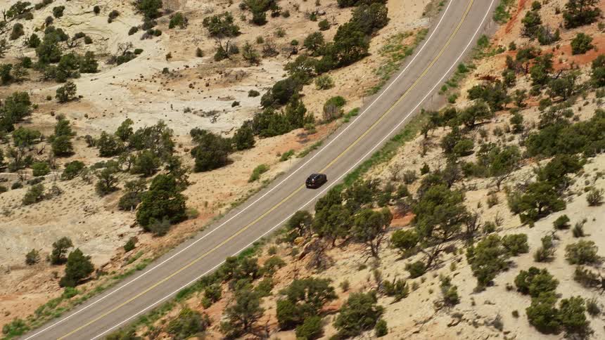  aerial footage of a black SUV driving on Route 12 Boulder Utah during daytime with partly cloudy skies