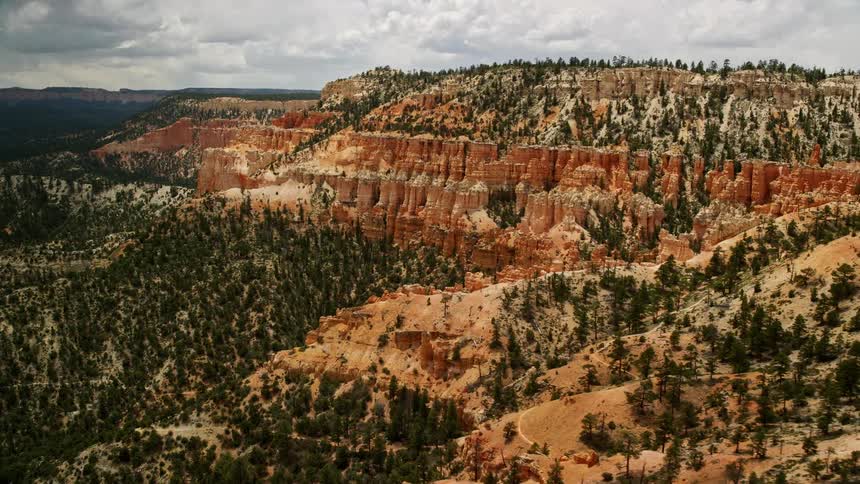  aerial footage reveals stunning Bryce Canyon National Park Utah showcasing hoodoos rocky mesa slopes and table mountains as the camera pans left amidst cloudy skies and breathtaking vistas