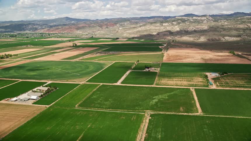 Aerial footage of farmland and brown hills in Richfield Utah during the summer showcasing the agricultural fields surrounded by a mountain range