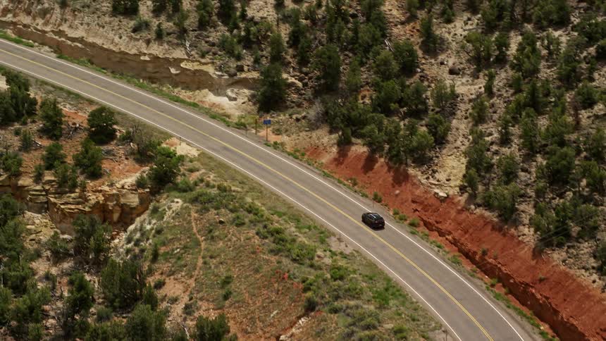 Aerial footage of a black SUV being tracked on Route 12 bend in Boulder Utah showcasing the scenic mountain road and partly cloudy skies during a sunny day in the Southwest United States